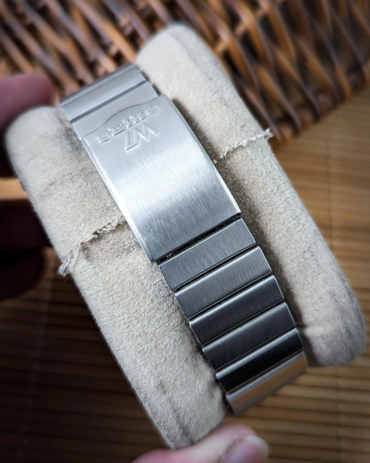 Stainless steel watch bracelet with clasp, embossed logo, displayed on cushion