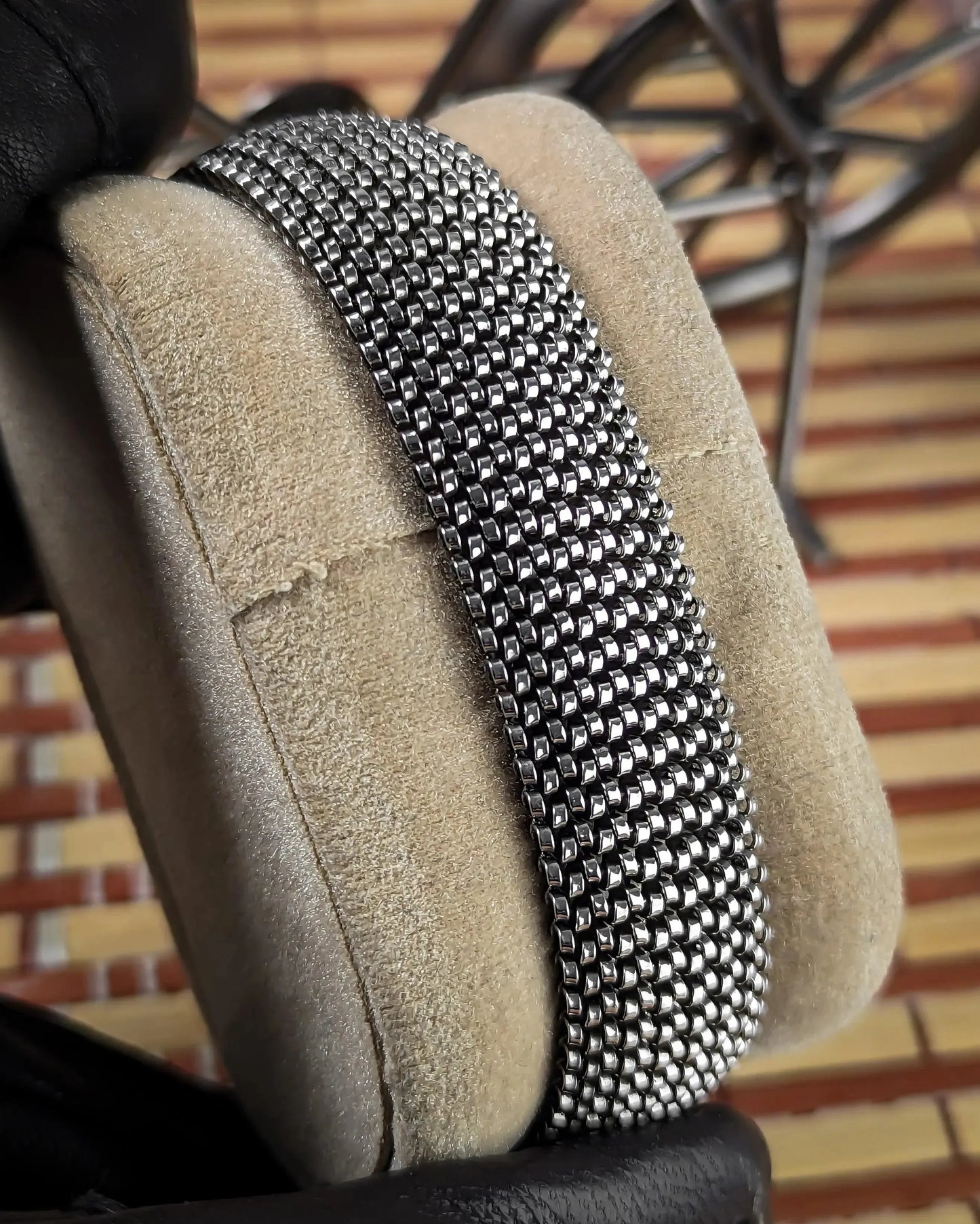 Close-up of a silver metal mesh bracelet displayed on a beige suede cushion