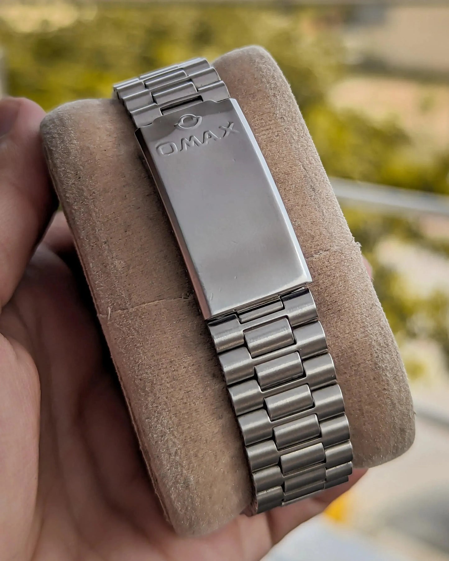 Stainless steel Omax watch bracelet clasp displayed on suede cushion outdoors