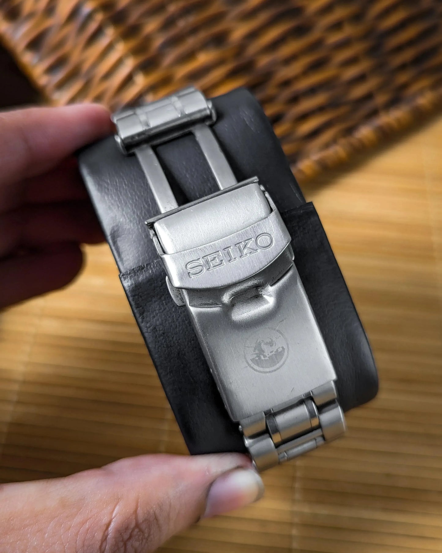 Close-up of Seiko stainless steel watch clasp on black cushion, hand holding bracelet
