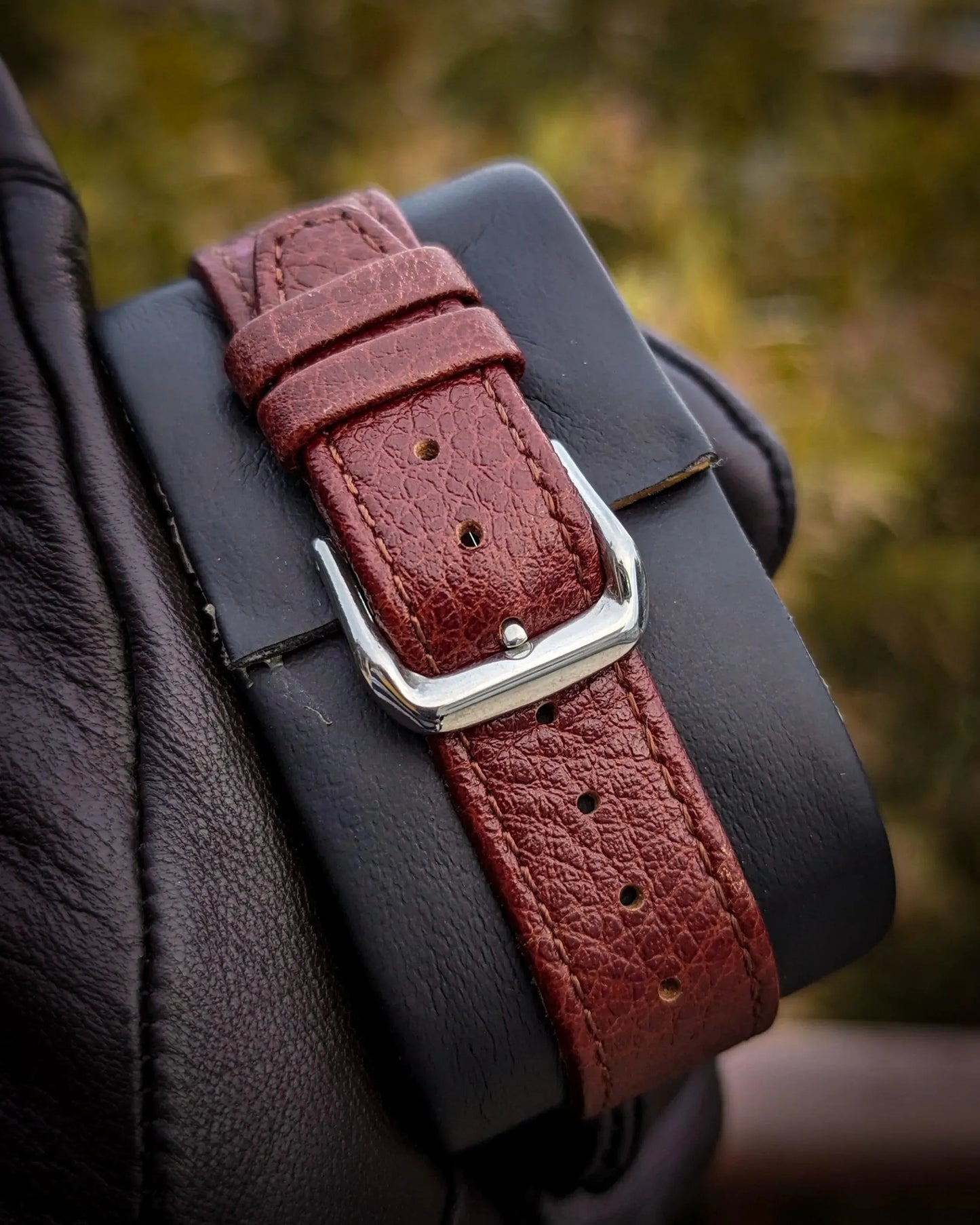 Close-up of a brown leather watch strap with silver buckle on a display cushion