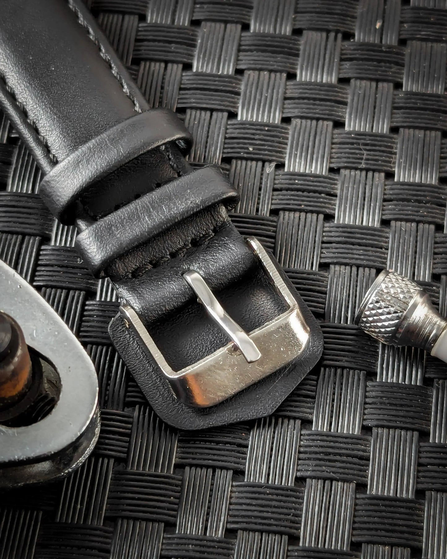 Black leather watch strap with silver buckle on textured surface, close-up detail