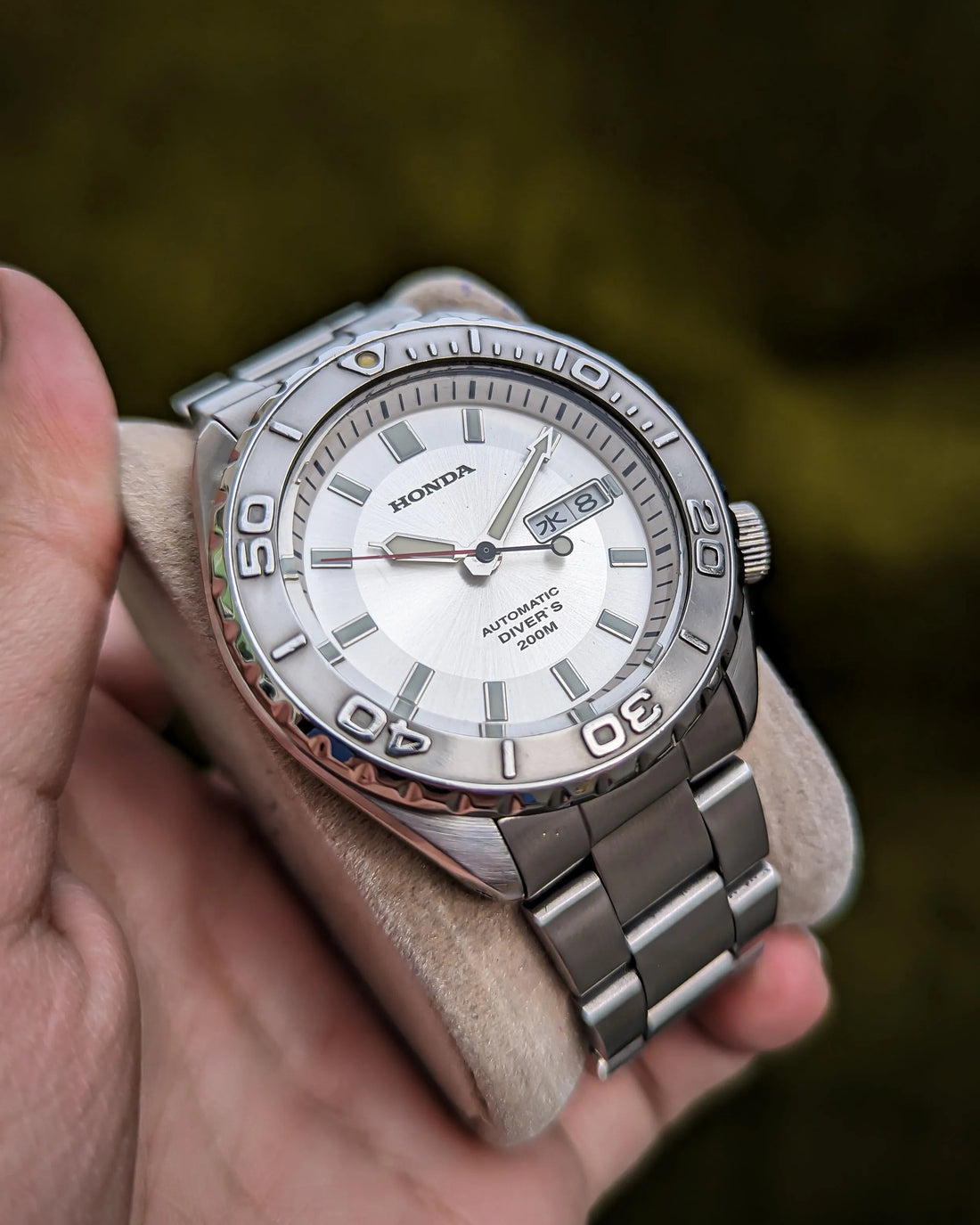 Silver automatic diver's watch with date display and stainless steel band held in hand