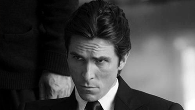 Man in black suit with serious expression sitting indoors, monochrome portrait