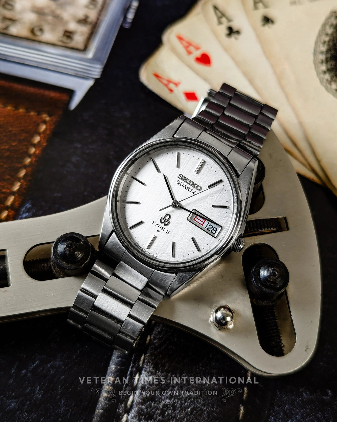 Silver Seiko quartz wristwatch with metal band, date window, surrounded by playing cards and tools.